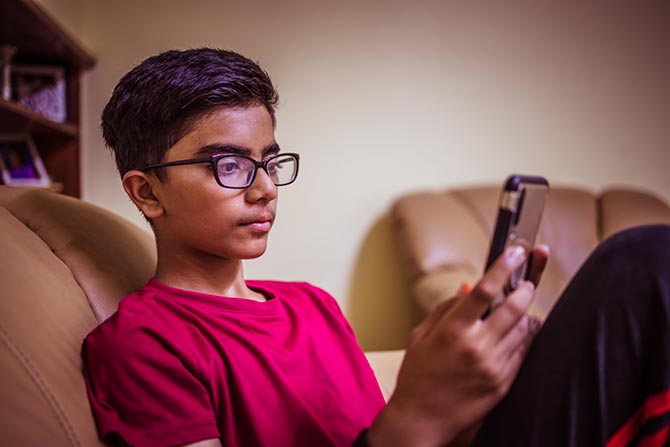 Jeune assis sur un divan avec un téléphone devant les yeux.